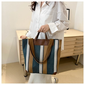 Detail of striped canvas tote bag with brown leather handles and reinforced corners