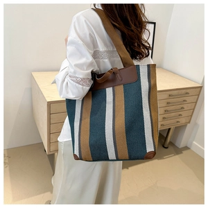 Detail of green striped canvas tote bag showing leather trim and wide shoulder strap