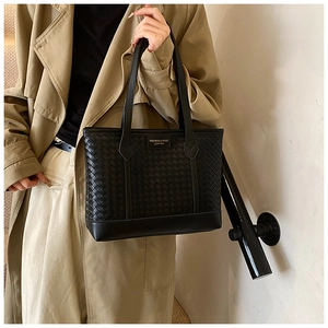 Detail of black woven tote bag featuring leather texture and fashion brand label