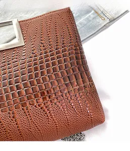 Detail of brown crocodile pattern handbag with silver hardware on denim background