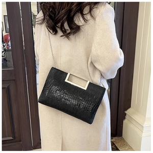 Close-up of black crocodile embossed handbag with silver metal handle on a beige coat