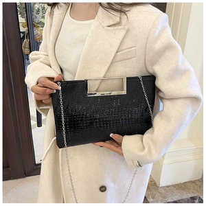 Detail of black crocodile pattern clutch bag with silver metal handle and chain