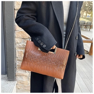 Detail view of brown crocodile texture leather handbag with elegant metal handle and chain