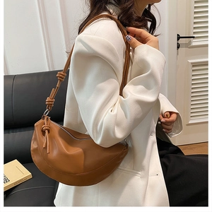 Sac demi-lune en cuir marron avec nœuds décoratifs sur la bandoulière porté par un mannequin