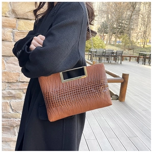 Close-up of brown crocodile texture handbag with rectangular metal handle and silver chain
