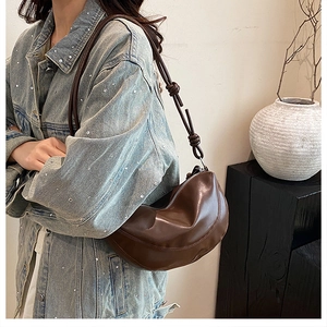 Détail d'un sac demi-lune marron café avec des nœuds décoratifs sur la bandoulière réglable