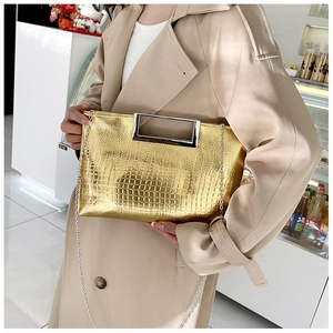 Detail of golden crocodile pattern handbag with metal handle and detachable chain strap