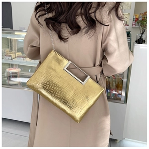 Detail of gold crocodile texture handbag with metallic handle and chain strap on trench coat