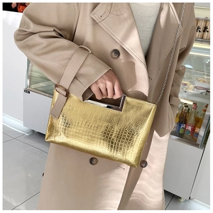 Detail of metallic gold crocodile embossed clutch bag with silver handle and chain strap