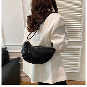 Détail du sac demi-lune noir avec fermeture éclair et gland sur un blazer blanc