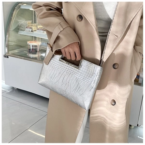 Silver crocodile texture handbag with metal handle worn with a beige trench coat