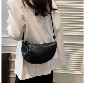 Détail du sac demi-lune noir avec nœuds décoratifs en cuir sur blazer blanc