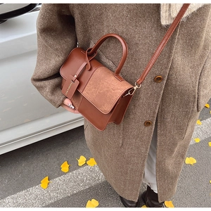 Detail of tan color-block handbag showing stitching and fashion pendant on autumn coat