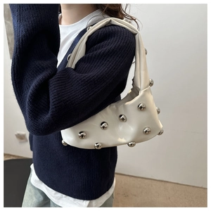 Detail of white half-moon underarm bag featuring decorative silver spherical metal rivets