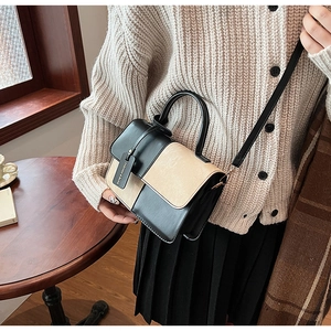 Detail of a chic two-tone crossbody bag in black and beige with a stylish hangtag accent