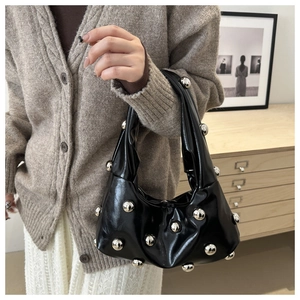 Detail of a black glossy underarm bag with silver spherical rivets held by a model