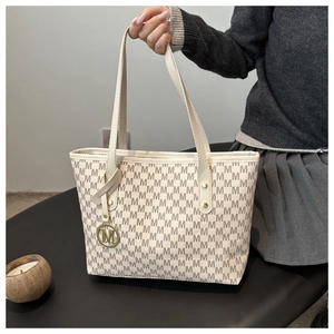 Detail of cream tote bag featuring grey M-pattern monogram and gold letter charm