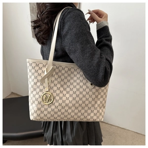 Close-up of beige tote bag with M letter print and golden circular metal charm