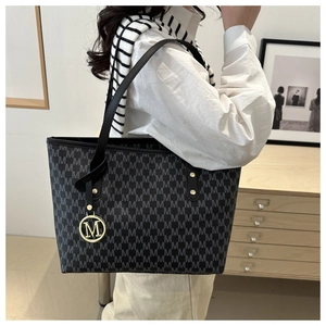 Detail shot of black tote bag featuring gray M pattern print and golden metal M charm