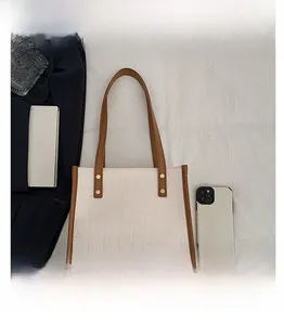 Detail of white crocodile embossed tote bag featuring brown straps and gold metal rivets