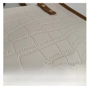 Macro detail of white crocodile embossed leather tote with golden rivets and brown trim