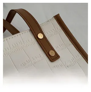 Detail shot of white croc-embossed leather bag with brown handle and golden hardware