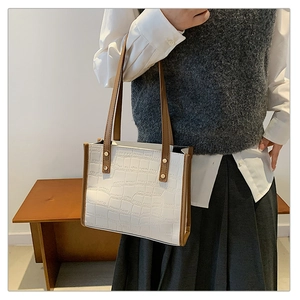 Detail of white crocodile pattern tote bag featuring contrast brown straps and gold rivets