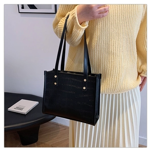 Detail of black crocodile-embossed tote bag featuring gold rivets and accordion side folds