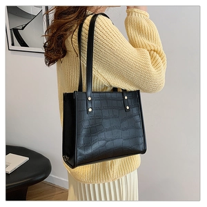 Detailed view of black crocodile pattern tote bag with gold studs on a shoulder strap