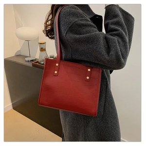 Detail of red crocodile pattern leather tote bag with gold rivets and slim straps