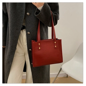 Detail shot of a red textured leather tote bag with gold rivets worn on shoulder