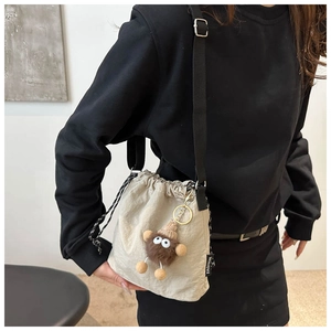 Detail of beige drawstring bucket bag featuring a plush brown monster charm and black strap