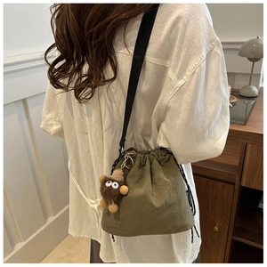 Detail of army green nylon bucket bag featuring a drawstring closure and plush doll charm