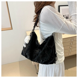 Detail of black pleated hobo shoulder bag featuring a white plush bear charm and metallic logo