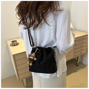 Detail of black drawstring bucket bag with bear pendant and woven shoulder strap