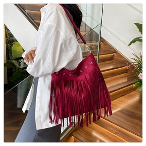 Detail of burgundy suede tote with silver eyelets and long fringe on wooden stairs