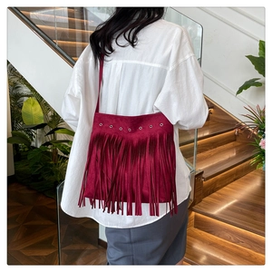 Detail of burgundy fringe shoulder bag showing suede texture and metallic eyelets on a model