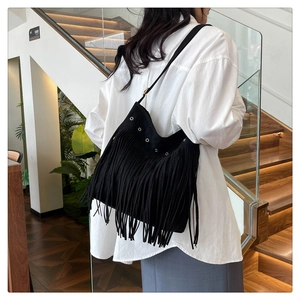 Detail view of black bohemian tassel shoulder bag with metallic eyelets on suede fabric