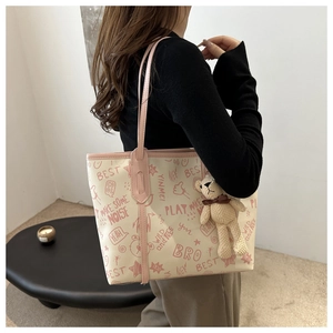 Close-up of cream tote bag with pink graffiti prints and a cute bear charm on shoulder