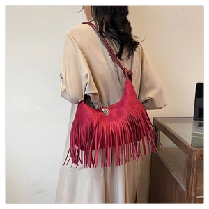 Gros plan d'un sac hobo rouge en daim à franges porté avec un trench-coat beige élégant