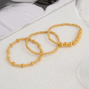 Detailed view of three-piece gold beaded stretch bracelets on a white textured fabric