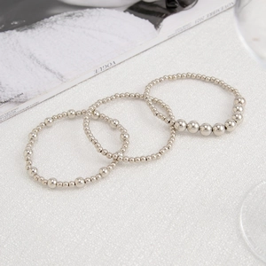 Detailed view of three-piece silver beaded bracelet set on a white textured background