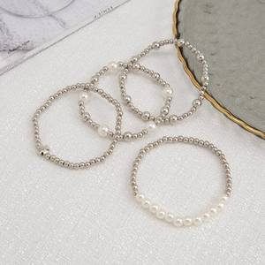 Detail of four-piece layered bracelet set with silver beads, pearls and cross pendant