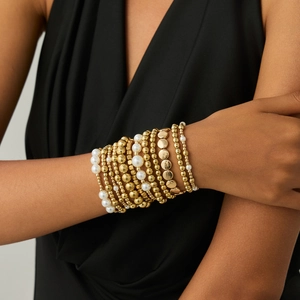 Detail of layered gold beaded and white pearl bracelet set on a female wrist