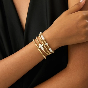 Detail of four-piece gold beaded bracelet set with white cross and pearl charms on wrist