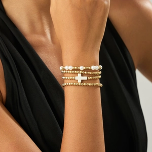 Detail of four-piece layered bracelet set with gold beads, white pearls and cross charm