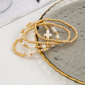 Detail of four-piece beaded bracelet set with gold beads, white pearls, and cross charms