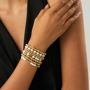 Close-up of layered gold beads and white pearl elastic bracelets set on a female wrist