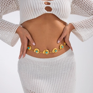 Détail d'une chaîne de taille bohème dorée avec turquoise sur une robe blanche