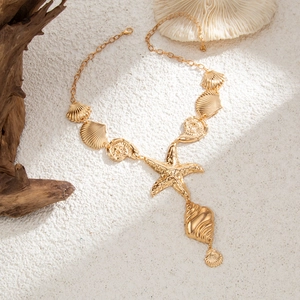 Dettaglio della collana con stella marina e conchiglie dorate su sfondo di sabbia bianca
